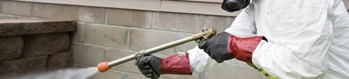 Pest control technician applying exterior insect treatment along a home foundation in Houston, TX
