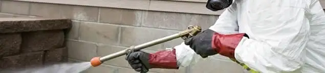 Pest control technician applying exterior insect treatment along a home foundation in Houston, TX