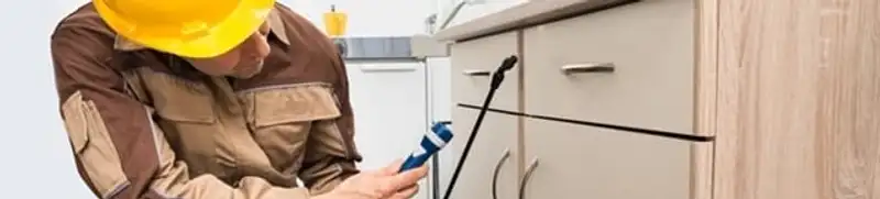 Roach exterminator applying treatment under kitchen cabinets in Houston, TX
