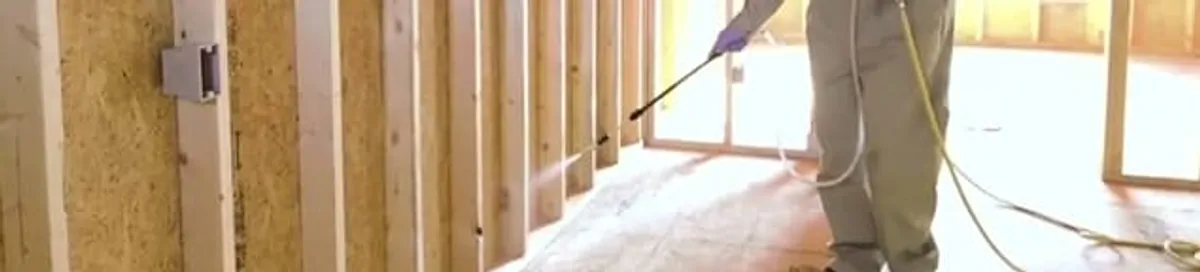 Termite treatment technician applying spray along framing and unfinished walls in Houston, TX