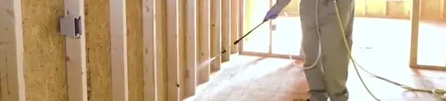 Termite treatment technician applying spray along framing and unfinished walls in Houston, TX